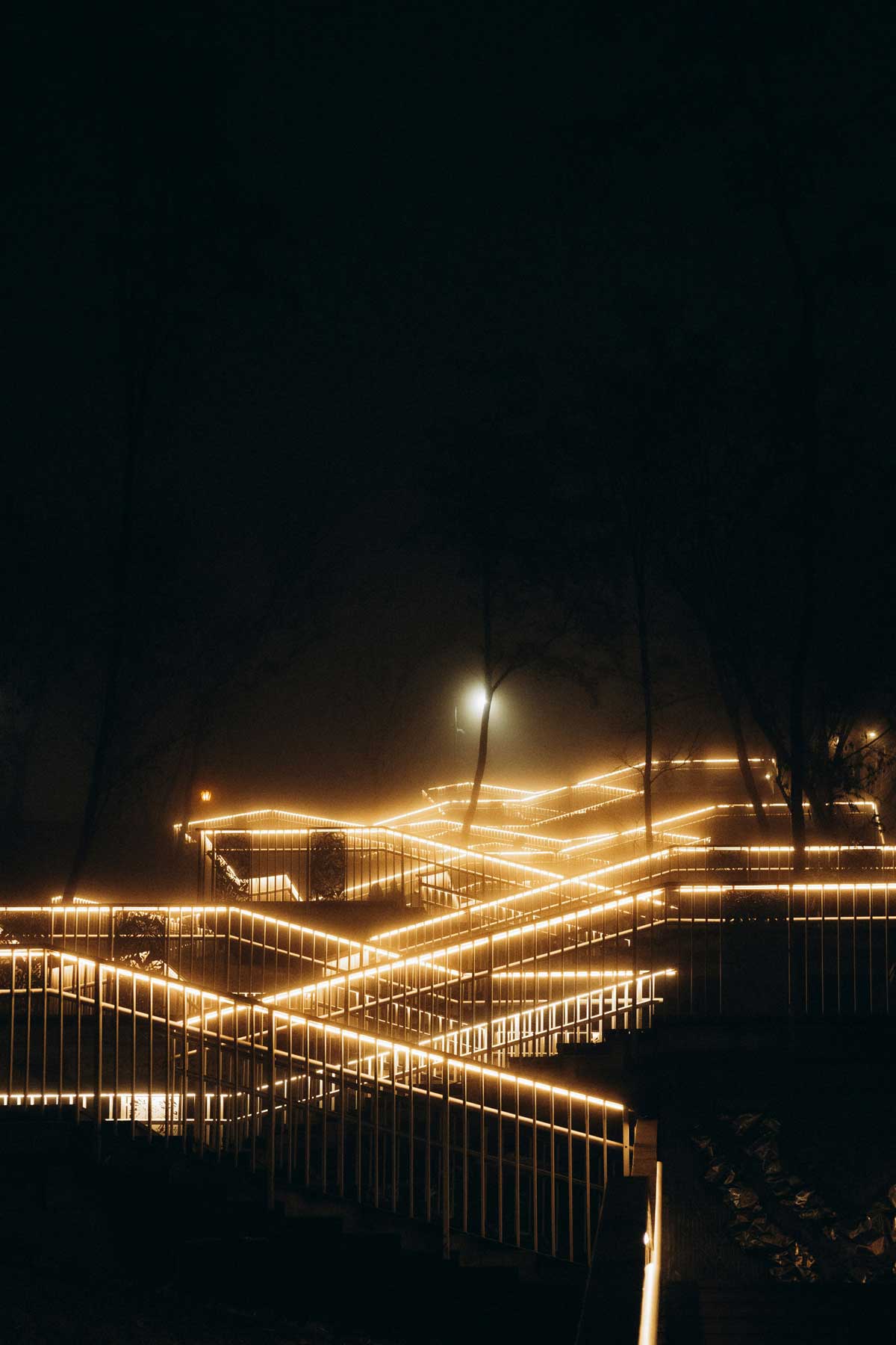 A zig zag path climbs into the distance. The path is surrounded by the dark and can only be seen because lights run along the handrails. At the top of the path a lone light shines dimly.